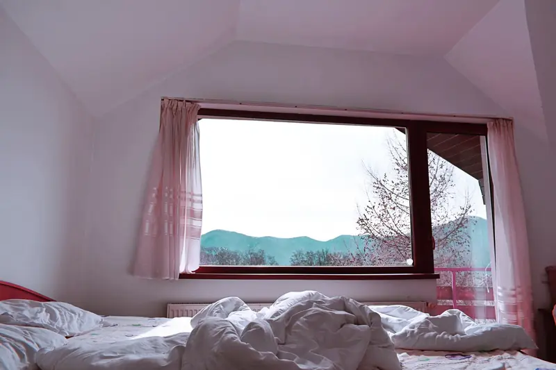 Bright bedroom interior with rumpled bed facing mountain view from window